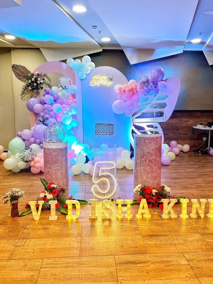 A dreamy pastel themed fifth birthday stage with a neon number "5", lit-up name letters, and cloud-like balloon arrangements.