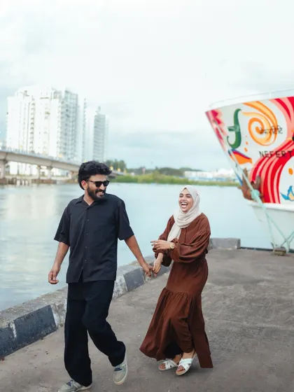 The couple shares a laugh while walking along the waterfront, a candid moment full of life and happiness.