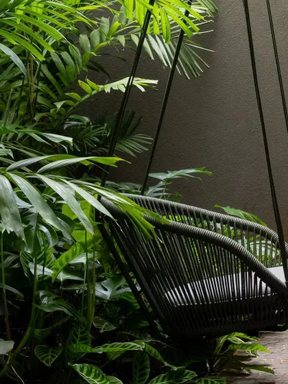 A modern hanging swing chair nestled among dense tropical foliage. We create these quiet corners within a larger garden to provide a private spot for reading and relaxation.