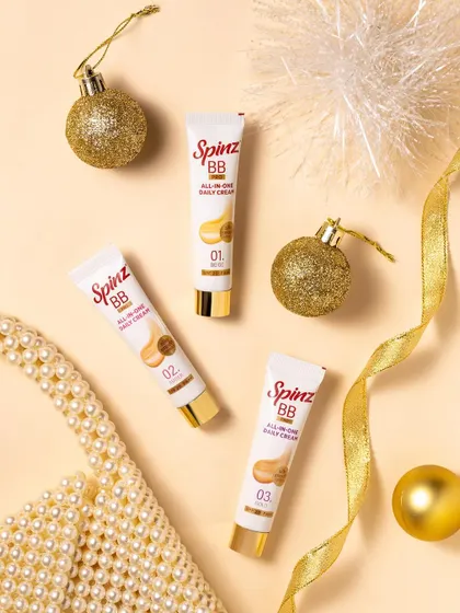 A Christmas-themed flat lay for Spinz BB cream. The gold ornaments and pearl accessories give the product a touch of holiday glamour.