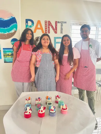 A group of four participants in aprons, standing behind a table neatly arranged with their candle creations.