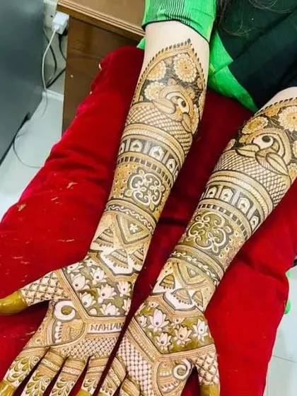 This design features the name 'Naman' on the palm, surrounded by lotus flowers. The arms have a unique pattern with bold peacock motifs.