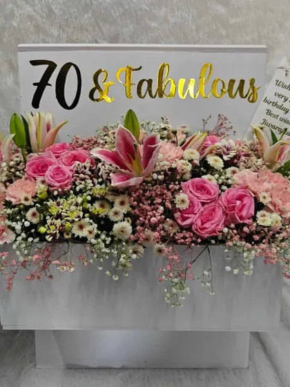 We don't do regular gifting. This "70 & Fabulous" floral box is overflowing with a lush arrangement of pink lilies, roses, and carnations, complete with a personalized birthday card.