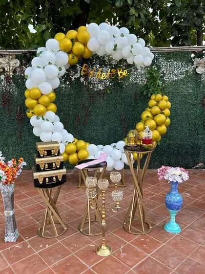 A 'Bride to Be' party setup with a circular balloon arch in yellow and white. The golden stands and candelabra add a touch of glamour to this outdoor celebration.