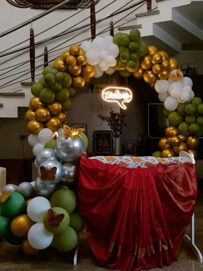 A beautiful and simple cradle decoration for a baby welcoming ceremony at home. The circular balloon arch in green, gold, and white, along with a 'Welcome' neon sign, creates a warm and inviting space.