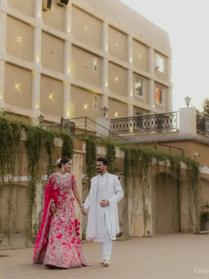 A graceful walking shot of the bride and groom in front of an elegant hotel, showcasing their beautiful outfits and the grandeur of the location.