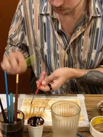 A participant at a coffee painting workshop, completely absorbed in his creation. These sessions offer a great way to get into a flow state.