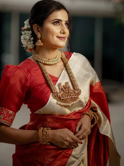 This is a look of pure bridal grace. Our model is adorned in a classic off-white and red Kancheevaram silk saree, complete with traditional temple jewelry and fragrant jasmine in her hair.
