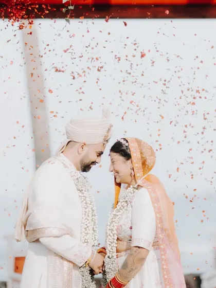 The same moment, closer up. The focus is entirely on the couple's intimate connection, their eyes closed, surrounded by a shower of red petals.