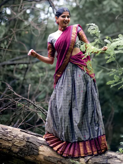 Balancing on a fallen log, this pose shows the versatility of a Kanchi half-saree for dynamic, nature-based photoshoots. The grey and magenta fabric stands out against the forest backdrop.