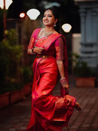 A full-length shot of the bride in her bright red saree, showing off her playful and confident personality. The bokeh from the lights in the background adds a dreamy quality.