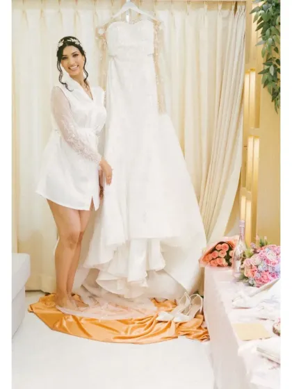 The bride in her robe, standing proudly next to her beautiful wedding gown. This is a classic and elegant getting-ready shot.