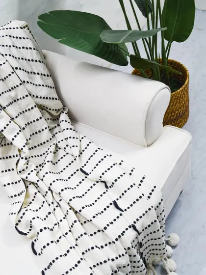 A detail shot of our custom 'Ivory Sofa,' showing the clean lines and the elegant throw with pom-pom details, perfect for a minimalist or modern home.