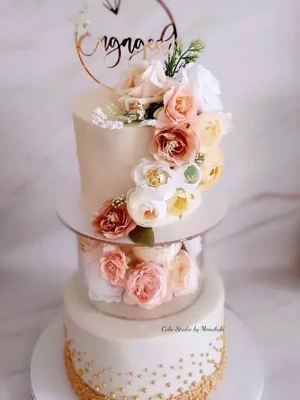 This floating tier engagement cake combines modern design with classic elegance. The bottom tier is dusted with gold sprinkles, and the entire cake is adorned with a cascade of peach and white flowers.