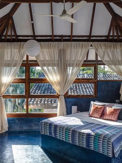 The Sky Room at Jalakara, featuring a seamless blue polished cement floor that extends to form the bed base. The room is designed as a pavilion in the trees, with large windows offering panoramic views.