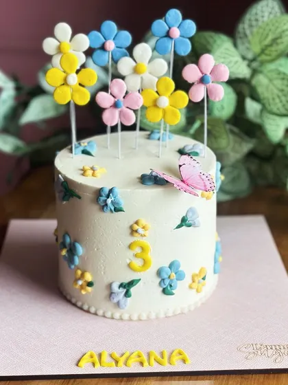 Blooming with sweetness. This floral cake is perfect for a third birthday, adorned with a garden of colorful, handcrafted sugar flowers and a delicate butterfly.