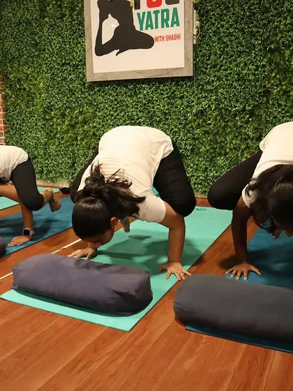 Using bolsters for support, these students work on their Bakasana (Crow Pose), building arm strength and balance.
