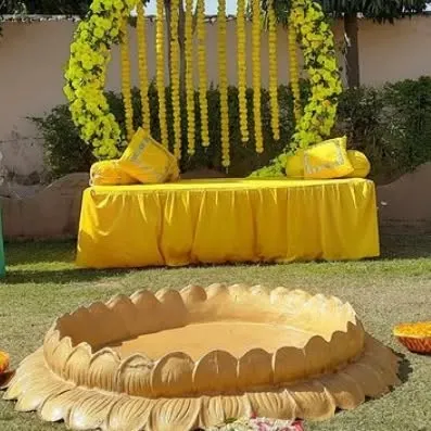 An outdoor Haldi seating area with a circular arch of yellow flowers and hanging marigold strings, creating a perfect photo spot.