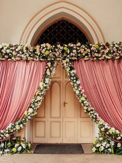 A grand doorway framed with pink drapes and a thick garland of pastel flowers, creating a dramatic and romantic entrance.