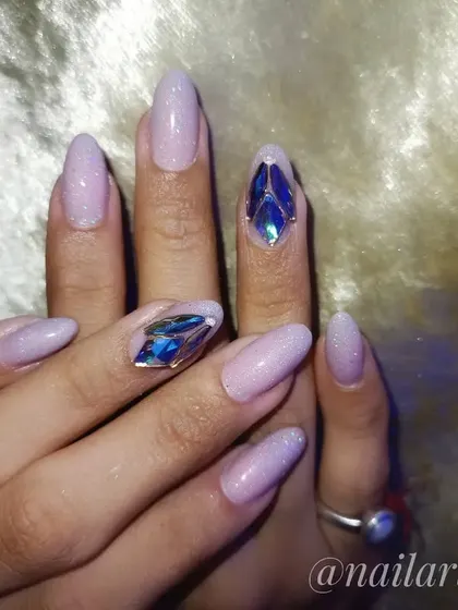 A glamorous New Year's Eve nail design. This set has a shimmery lavender base with large, diamond-like blue rhinestones for a dramatic, icy look.