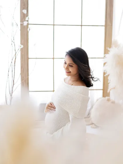 Lit by love, growing with grace. A serene portrait of a mom-to-be in a cozy white knit dress, bathed in soft window light.