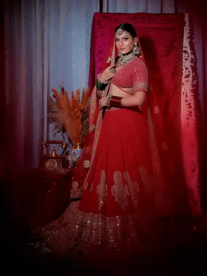 A three-quarter shot of the bride posing confidently in her red lehenga. The composition includes traditional elements like a decorative pot, adding context to the bridal shoot.