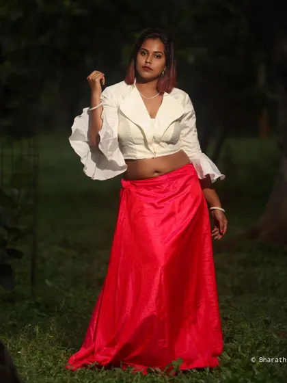 A fashion-forward portrait in a park setting. The contrast between the bright red skirt and the dark green background is striking.