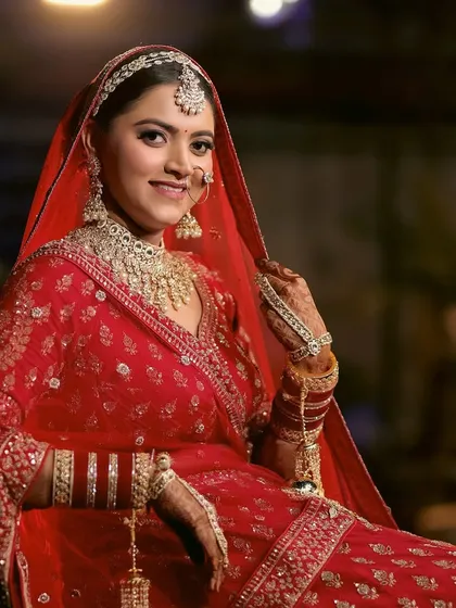 A classic, smiling portrait of a bride in her traditional red wedding attire. The photo captures her happiness and the beautiful details of her bridal look.