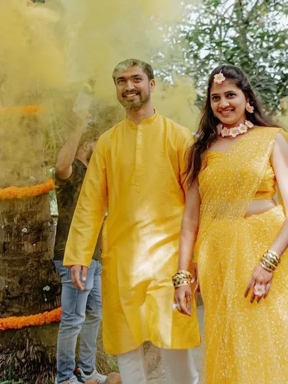 The couple is all smiles as they are welcomed with a burst of yellow color smoke, adding a touch of modern fun to their traditional Haldi ceremony.