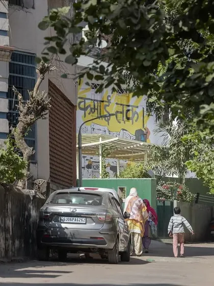 A view from the street shows local residents walking towards the Basera Community Plaza. Its accessible design makes it a natural part of the neighborhood's daily life and circulation paths.
