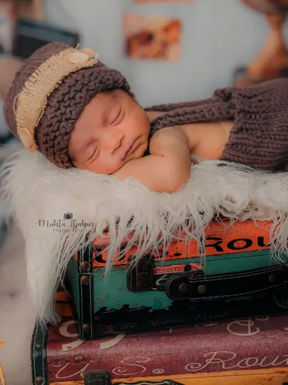 This image captures the newborn in a peaceful slumber, highlighting the textures of the fur blanket and the rustic suitcases. A perfect memory of a tiny explorer.