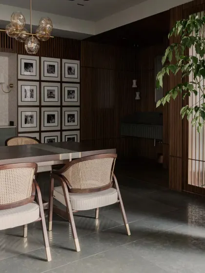 A dining area that feels both formal and inviting. The combination of cane-back chairs, a modern glass chandelier, and a gallery wall of family photos creates a space that is personal and elegant.