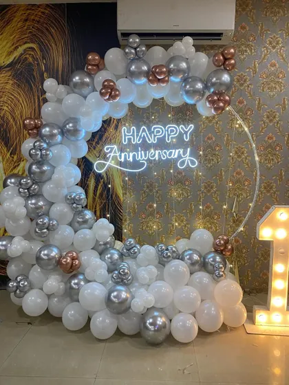 A stylish first-anniversary setup with a balloon ring in white, silver, and rose gold, a neon sign, and a light-up number "1".