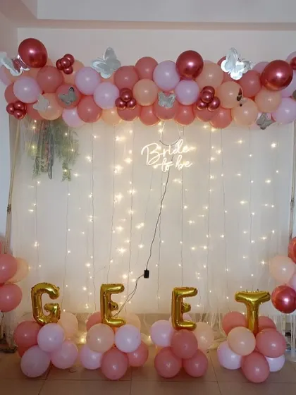 This bridal shower decoration features a balloon garland over a backdrop of sheer curtains and fairy lights. The "Bride to be" neon sign adds a modern glow, and I can spell out names or words with foil balloons, as seen here.