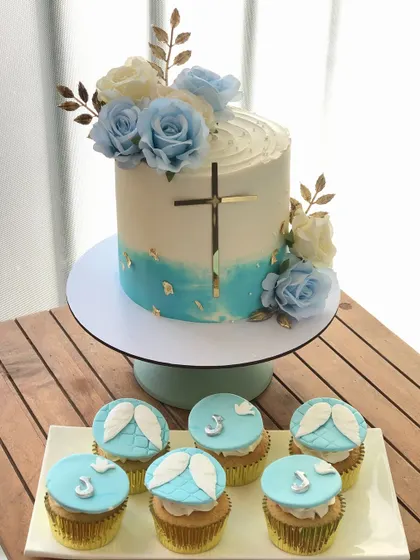 A baptism cake and cupcake set in a lovely blue and white theme, decorated with angel wings and crosses.