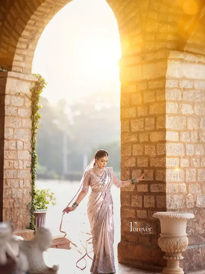 The bride in a sun-drenched archway. The light catches the delicate embroidery on her saree and blouse, creating a magical and ethereal effect.