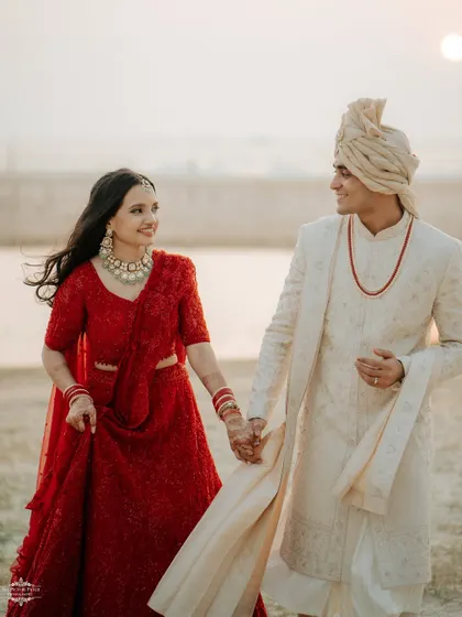 A beautiful shot of the couple walking by the water at sunset, their red and white outfits creating a stunning contrast.