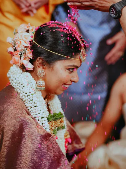 A beautiful side profile of the bride as she receives blessings during the Akshate ritual, with colorful rice grains showering down on her.