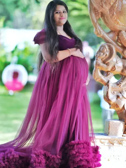 An outdoor shot featuring a beautiful magenta tulle gown with a ruffled hem. The natural light and garden setting complement the soft, flowing fabric of the dress.