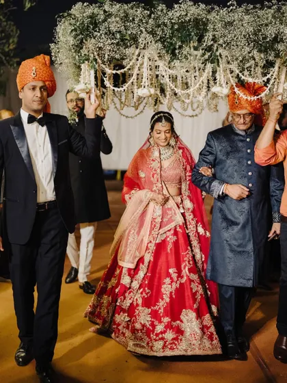 The bride's grand entrance, walking down the aisle with her father and brother under a beautiful phoolon ki chadar.