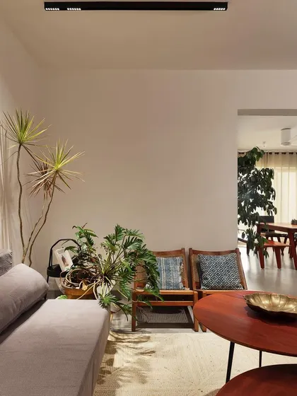 The living room of the 'Rustic Minimal' apartment, showing the transition into the dining area. The open layout and consistent use of natural materials and plants create a cohesive and flowing living space.