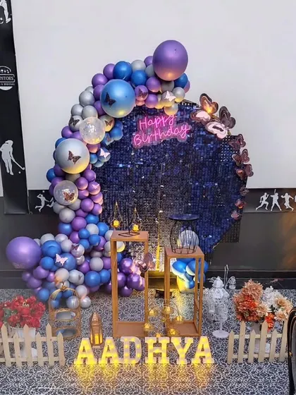 A crescent-shaped balloon arrangement on a deep blue sequin backdrop, accented with butterflies, creates a magical, starry-night effect.