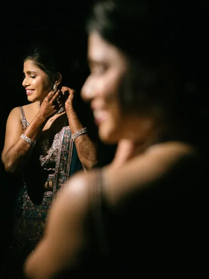 A beautiful, artistic shot of the bride getting ready. This moment captures her smile as she puts on her earrings, with her reflection showing the complete, elegant look.