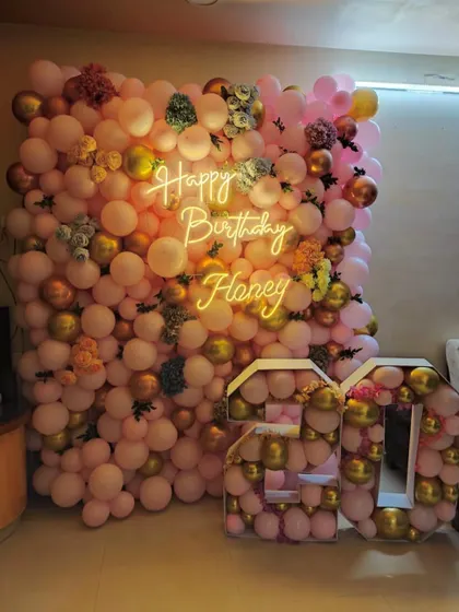 I can turn any room in your home into a beautiful party space. This 20th birthday at-home decoration features a full wall of pink and gold balloons, accented with flowers, a custom neon sign, and large balloon-filled marquee numbers.