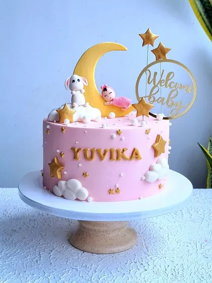 A full view of the "Welcome Baby" cake on its stand.