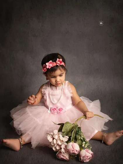 A sweet and simple portrait of a birthday girl in a pink dress, sitting with a bouquet of flowers against a classic grey backdrop.