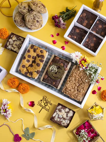 A beautiful flat lay of a Raksha Bandhan dessert tray, featuring an assortment of brownies, cookies, and festive decor on a bright yellow background.