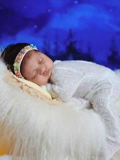 A close-up view of the 'dreaming on the moon' theme, showing the baby peacefully sleeping in a white knit outfit on a soft fur blanket.