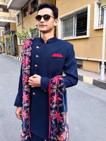 This trendy navy blue Indo-Western sherwani is a versatile choice for any festive occasion. The printed velvet stole adds a luxurious and stylish touch.