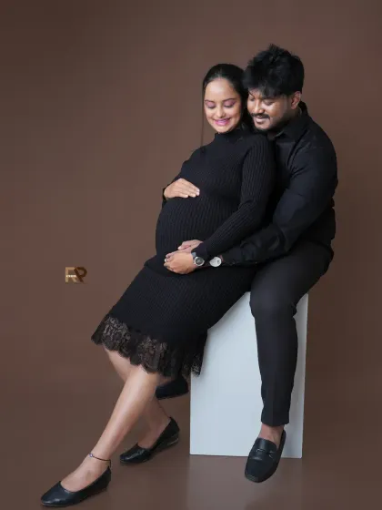 A beautiful seated portrait of a couple. The mom-to-be looks radiant in her black bodycon dress, sharing an intimate moment with her partner.
